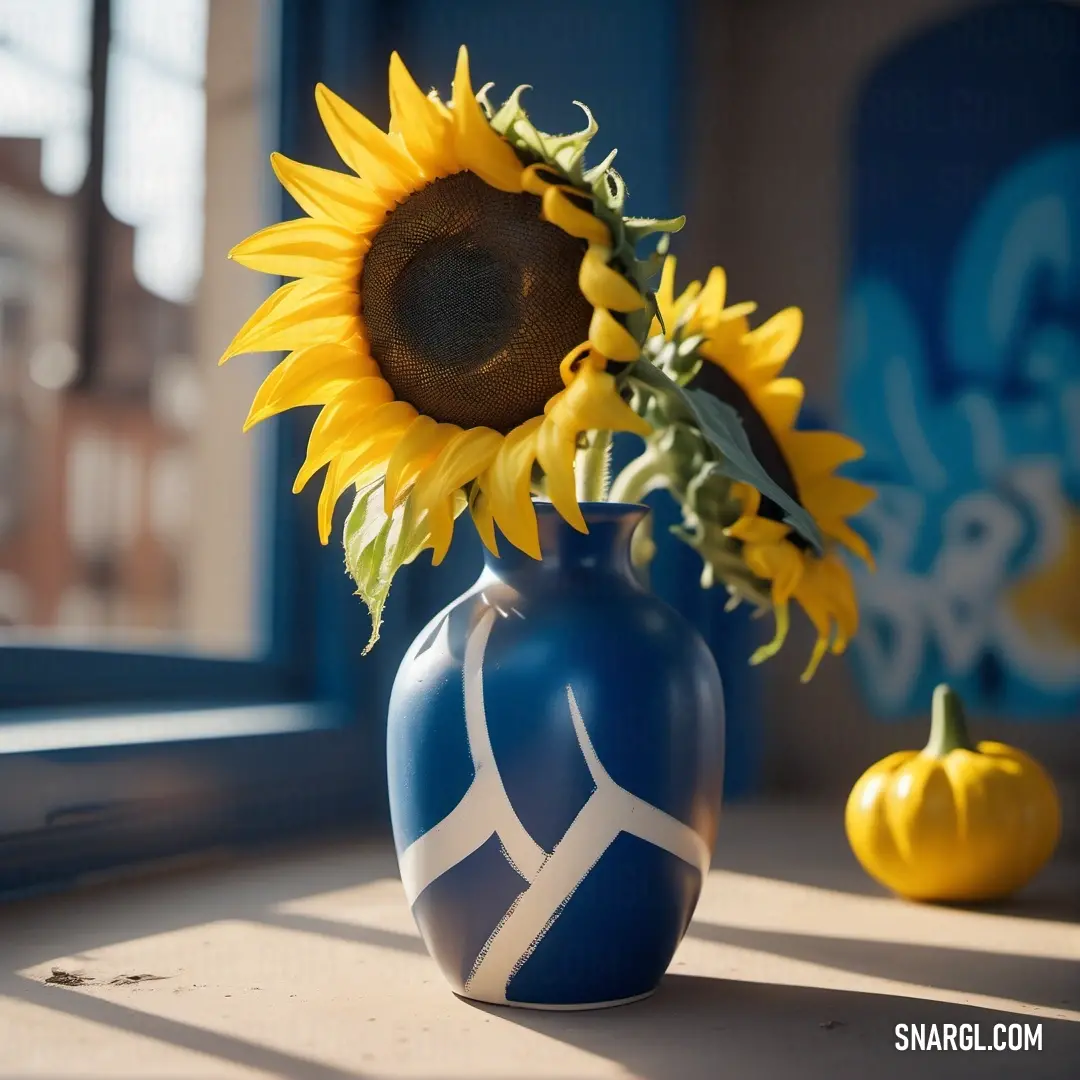 Blue vase with a sunflower and a pumpkin in it on a window sill with a blue and white striped vase. Example of CMYK 0,16,100,0 color.