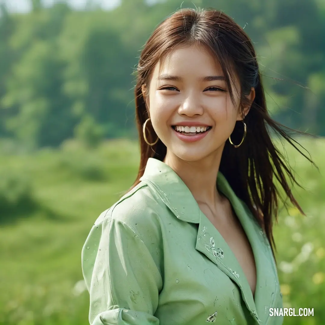 Woman with long hair smiling in a field of grass and flowers with trees in the background. Example of Granny Smith Apple color.