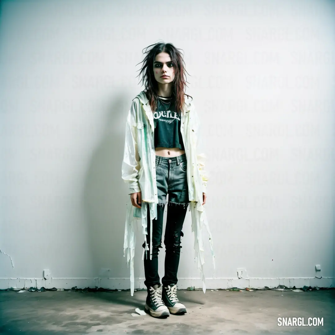 Woman standing in front of a white wall wearing a jacket and black pants with fringes on it