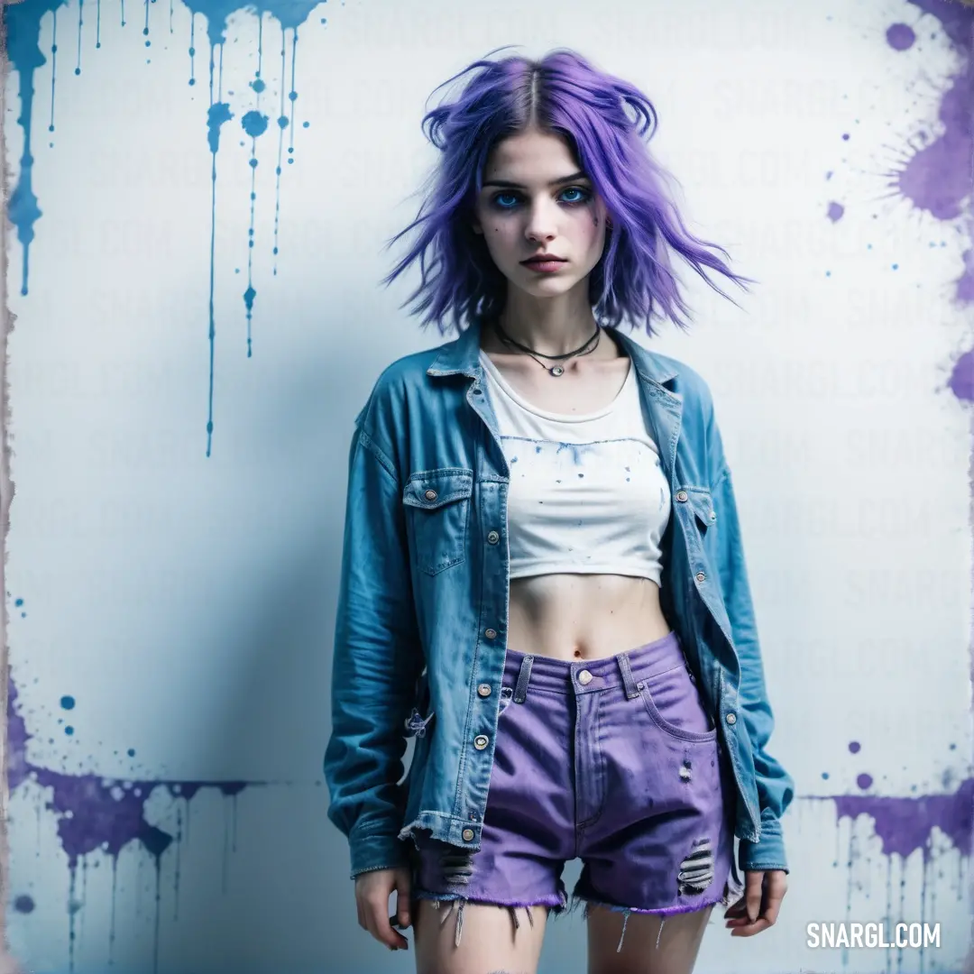 Woman with purple hair and a denim jacket on posing for a picture with a blue background and purple paint splattered on the wall