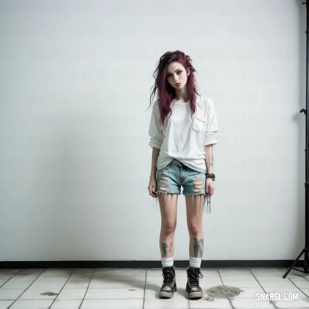 Woman with red hair and tattoos standing in a room with a white wall and a black