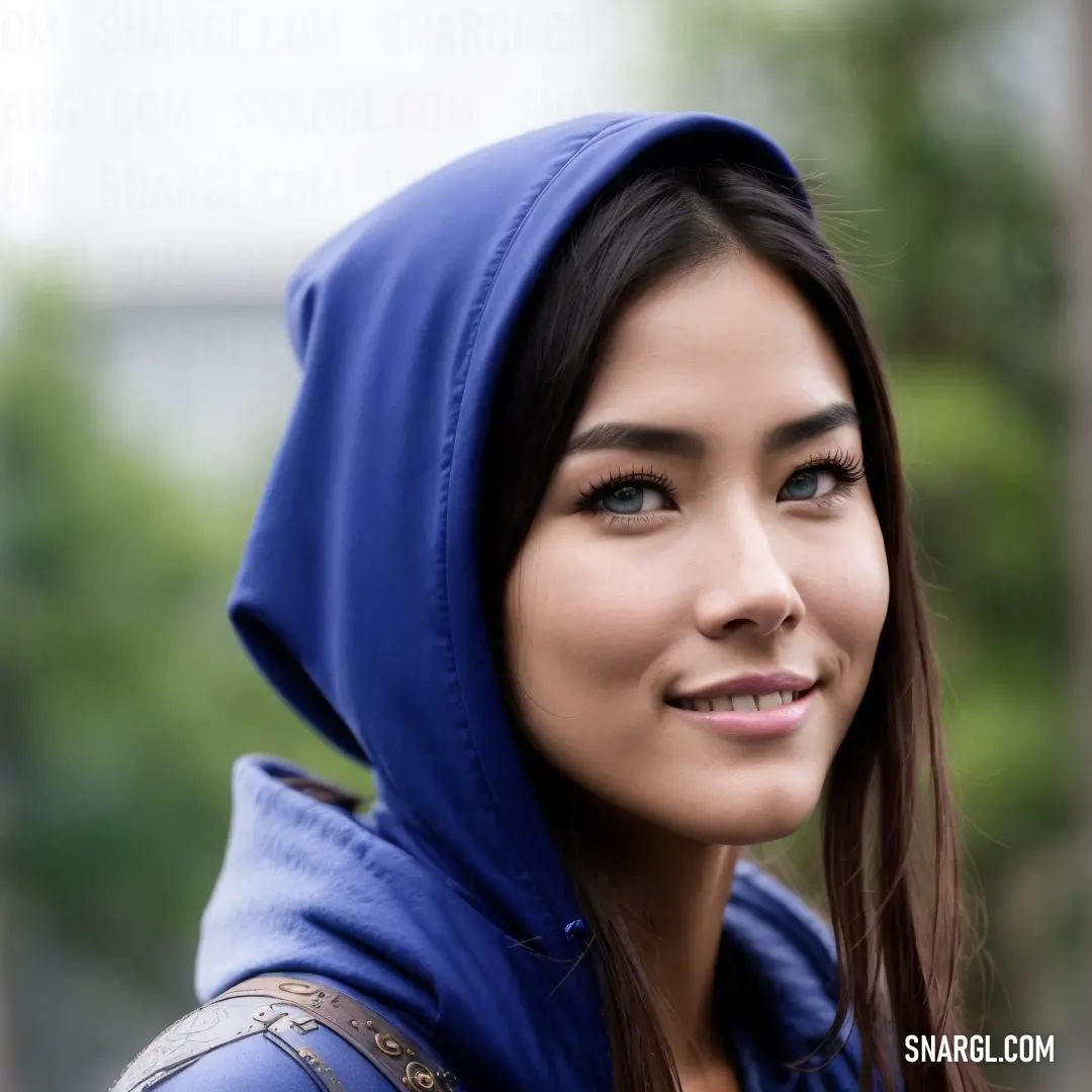 Woman in a blue hoodie is smiling for the camera with a smile on her face and a tree in the background