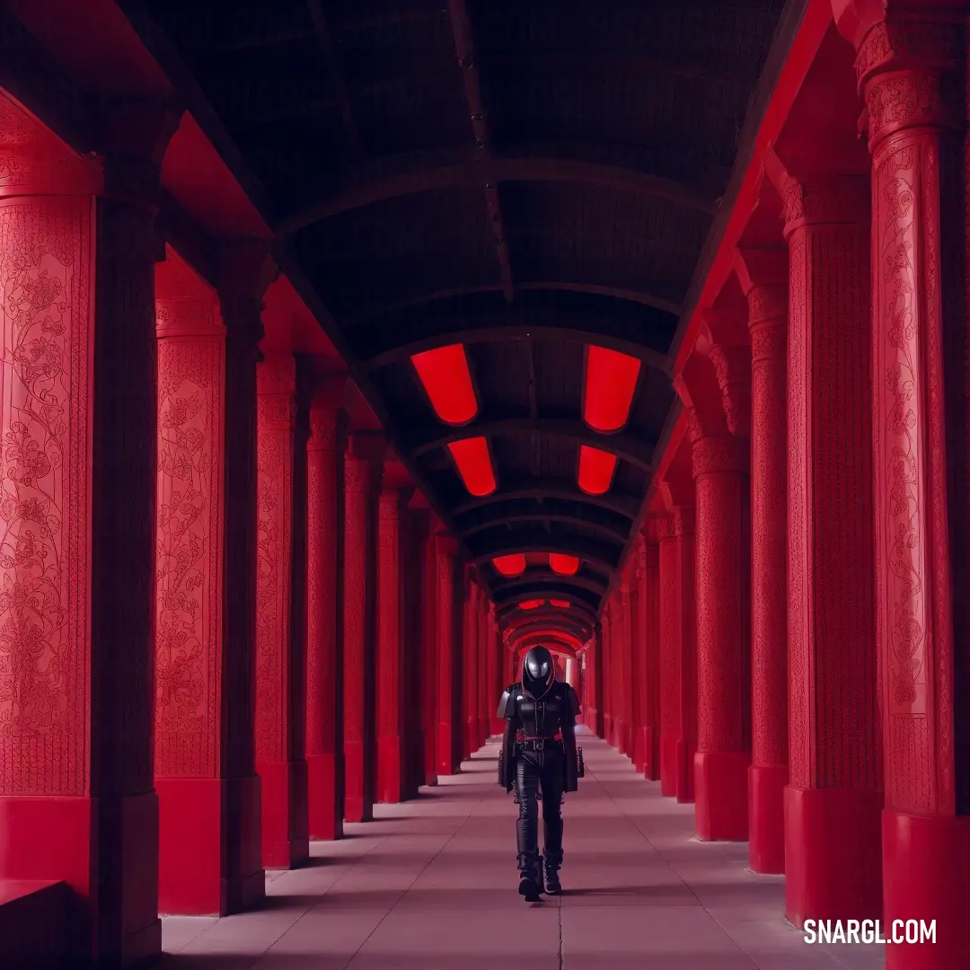 Man walking down a long hallway with red columns on both sides of it and a red light on the ceiling