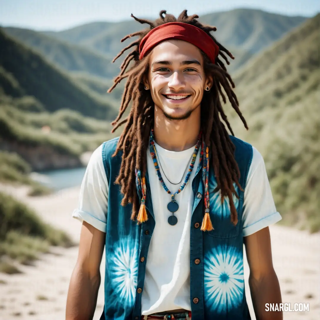 Man with dreadlocks and a bandana smiles at the camera while standing in a desert area