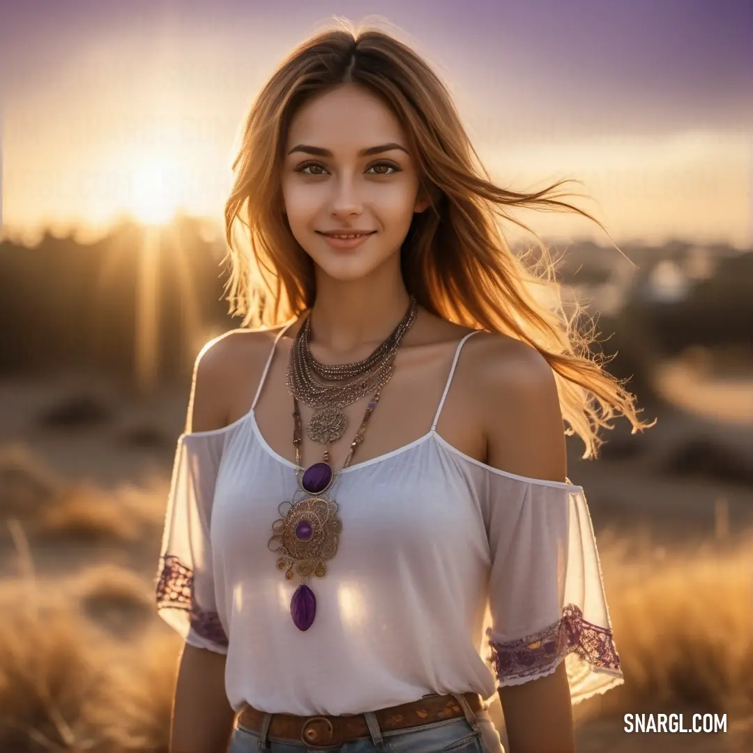 Woman with a necklace and a white shirt is standing in a field at sunset with the sun behind her