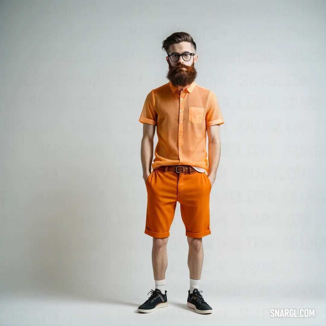 Man with a beard and glasses standing in a studio photo wearing orange shorts and a shirt with a button down