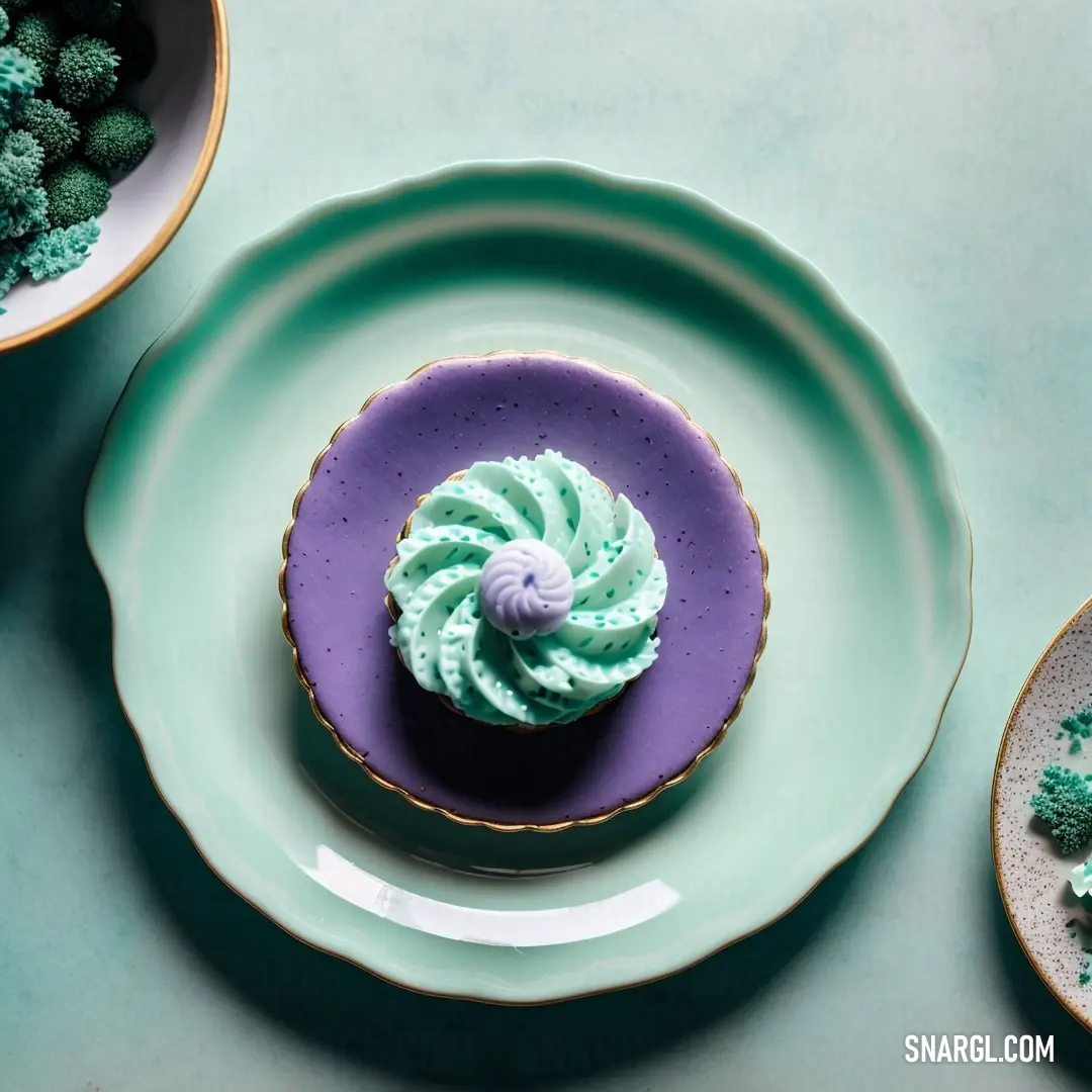 Cupcake with green frosting on a plate next to other plates of food on a table top