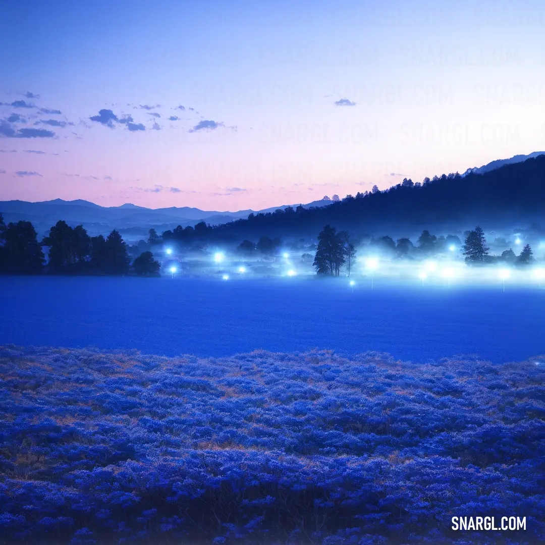 Field with a mountain in the background and cars driving on it at night time with fog in the air