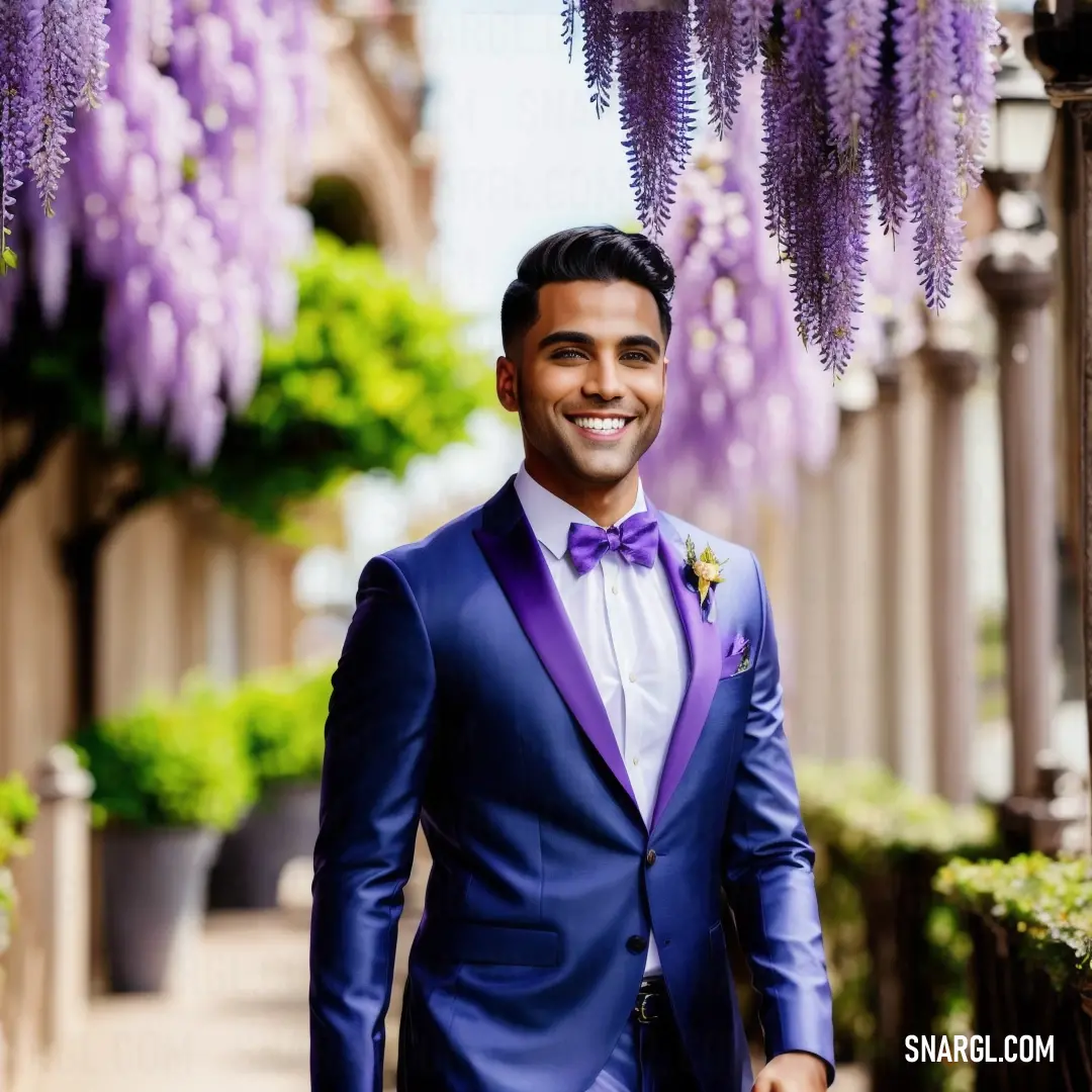Man in a purple suit and bow tie standing under a purple flower tree in a city street with a building in the background