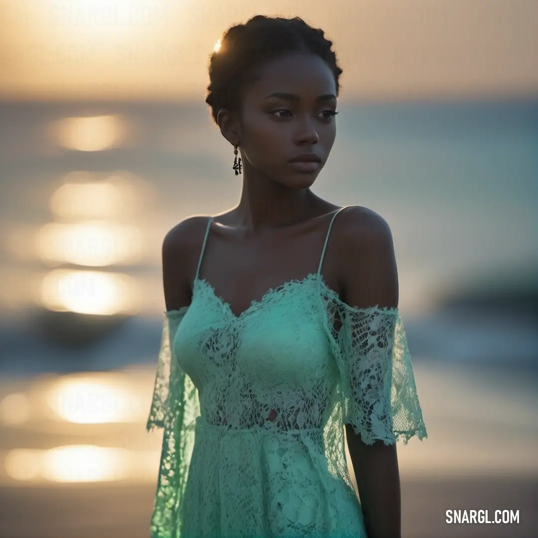 Woman in a green dress standing on a beach at sunset with the sun behind her and the ocean in the background
