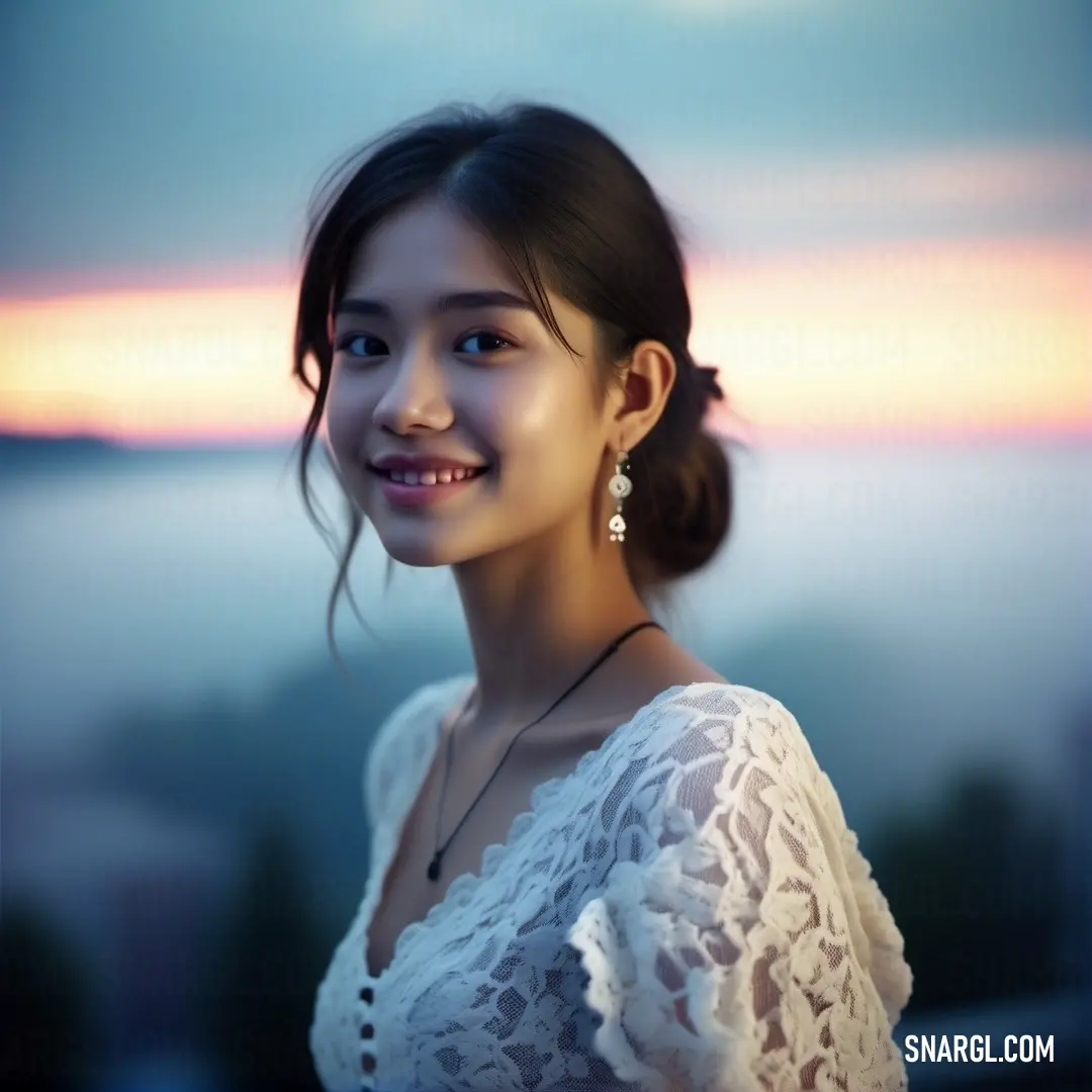 Woman with a white shirt and a necklace on smiling at the camera with a sunset in the background