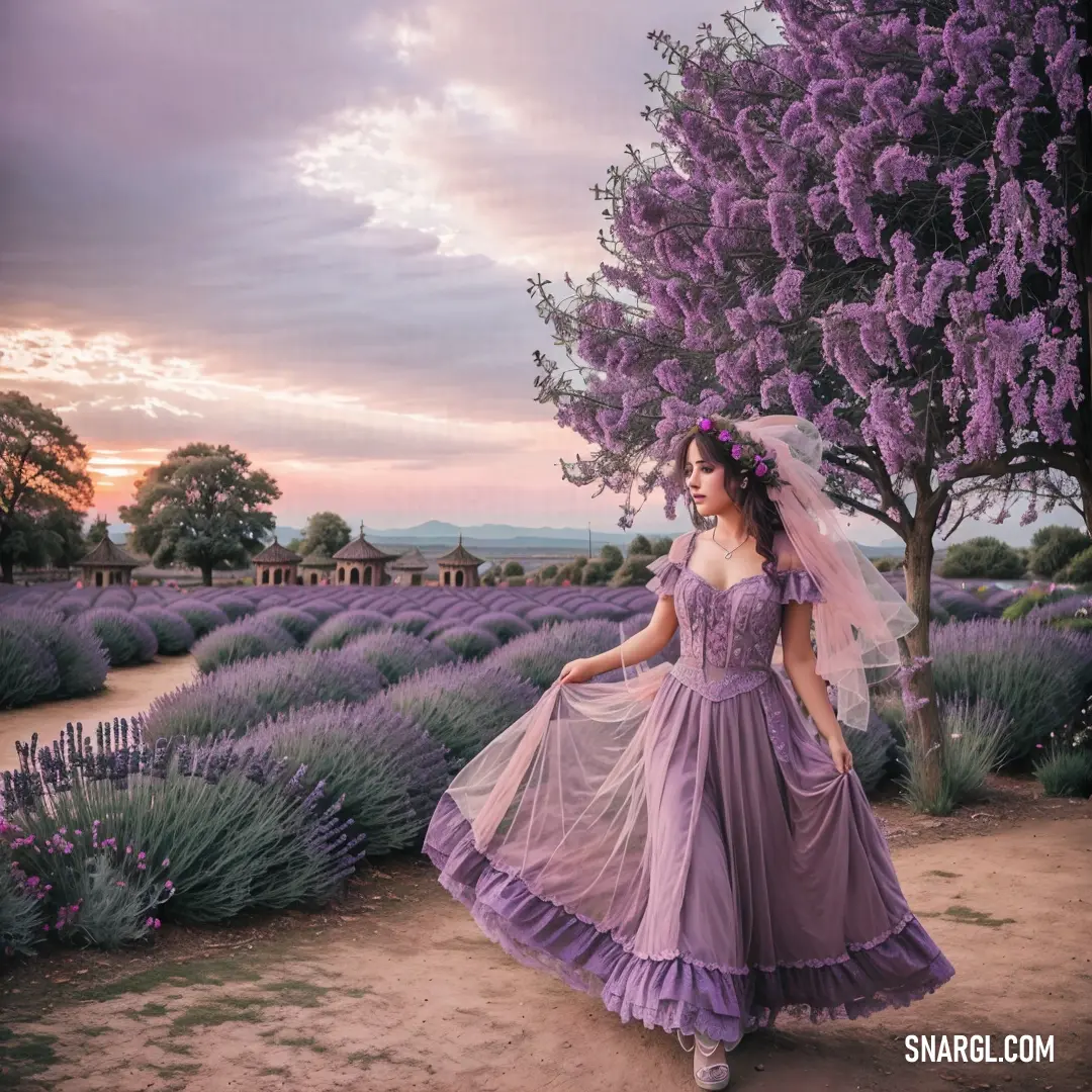 Woman in a dress and veil standing in a lavender field at sunset with a tree in the background