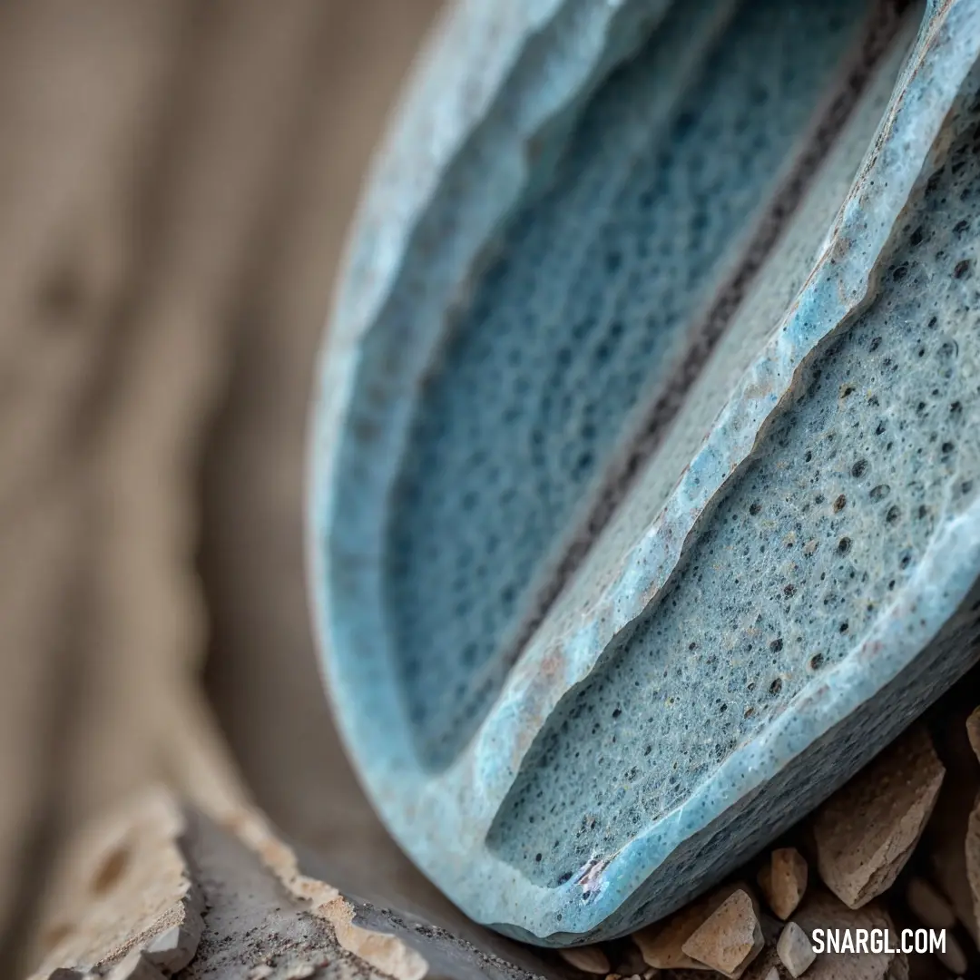 Close up of a blue vase on a rock pile of rocks and gravel with a brown background and a small white object