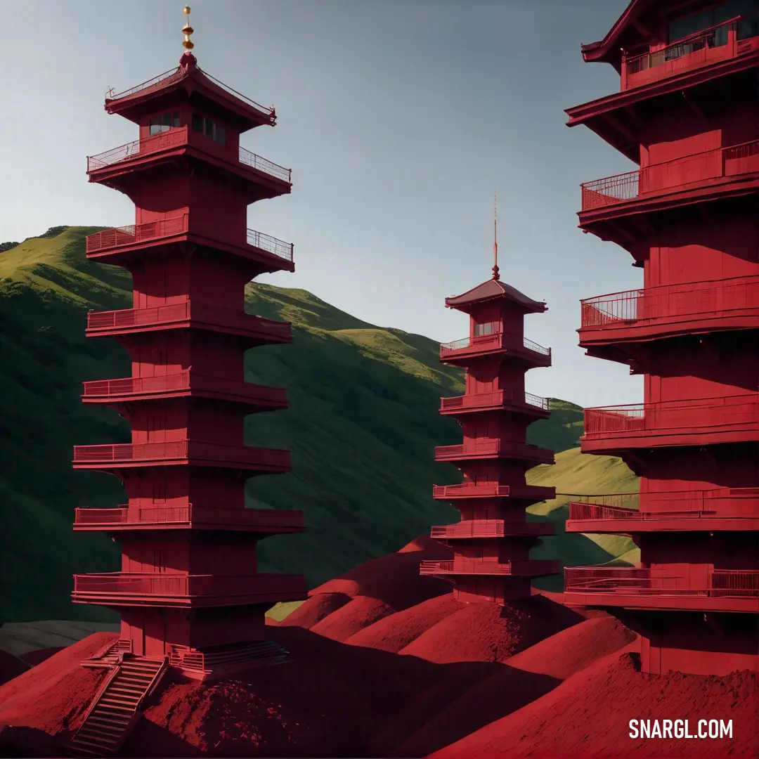 Group of red towers on top of a hillside next to a green hillside with a mountain in the background. Color #800000.
