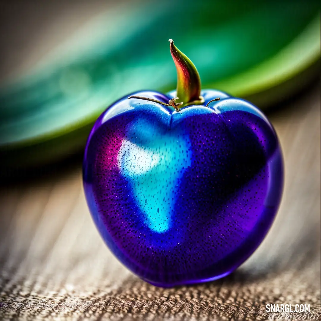 Shiny blue apple on top of a table next to a green plate on a table cloth