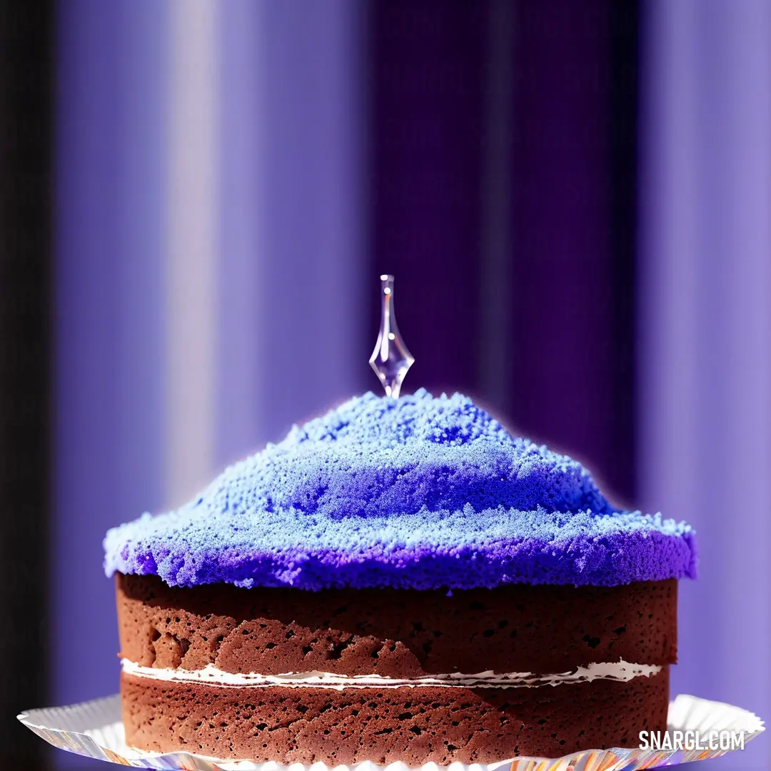 Cake with blue frosting on a plate on a table with a purple curtain behind it and a small silver object on top