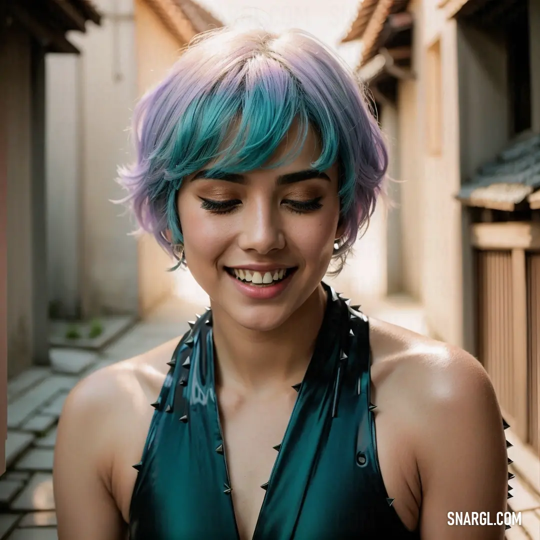 Woman with blue and purple hair smiling at the camera while wearing a green top and black leather collar