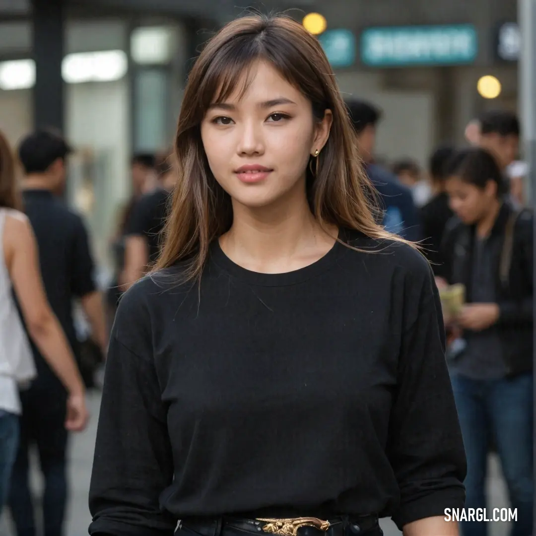 Woman standing in front of a crowd of people wearing black clothing and a black top with a gold belt