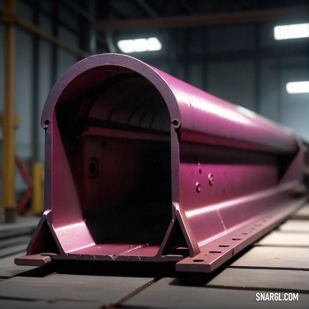 Pink metal object on top of a wooden floor in a warehouse area with lights on the ceiling. Example of #C54B8C color.