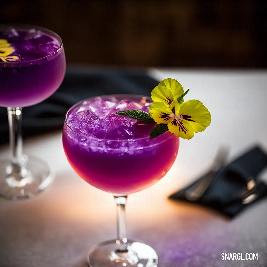 Two glasses of purple liquid with a flower on top of them on a table with a napkin and a fork