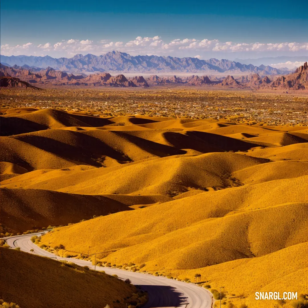 Winding road in the middle of a desert with mountains in the background and a blue sky with clouds