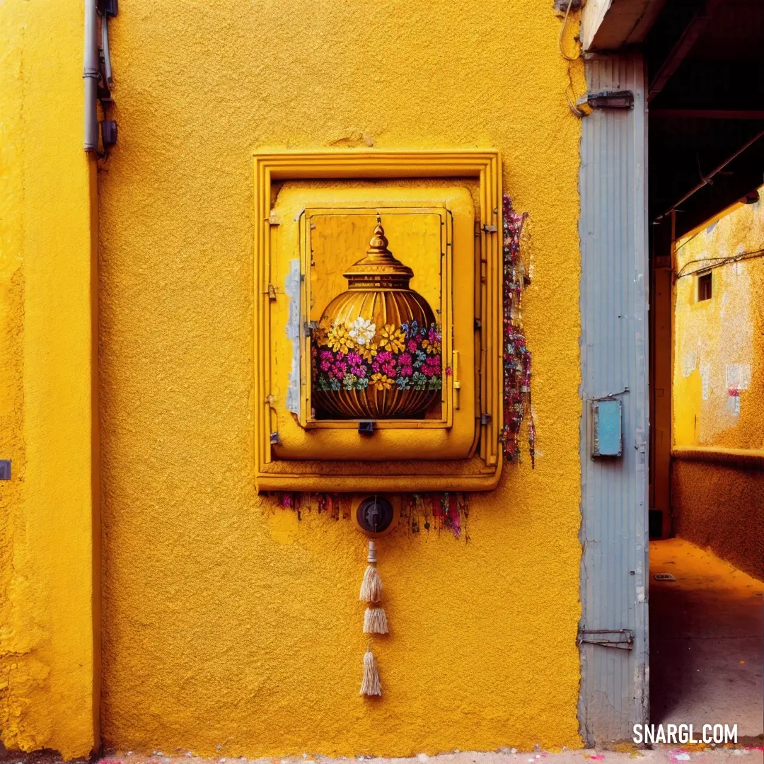 Yellow wall with a picture of a vase on it and a tassel hanging from the side of it