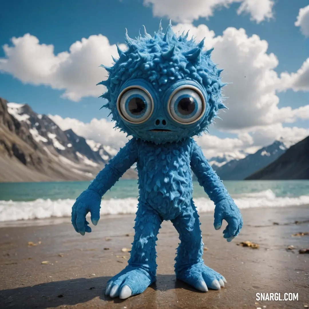 An adorable blue stuffed animal with oversized eyes stands proudly on a picturesque beach, framed by majestic mountains and beneath a soft, cloudy sky, evoking a sense of serenity and wonder.