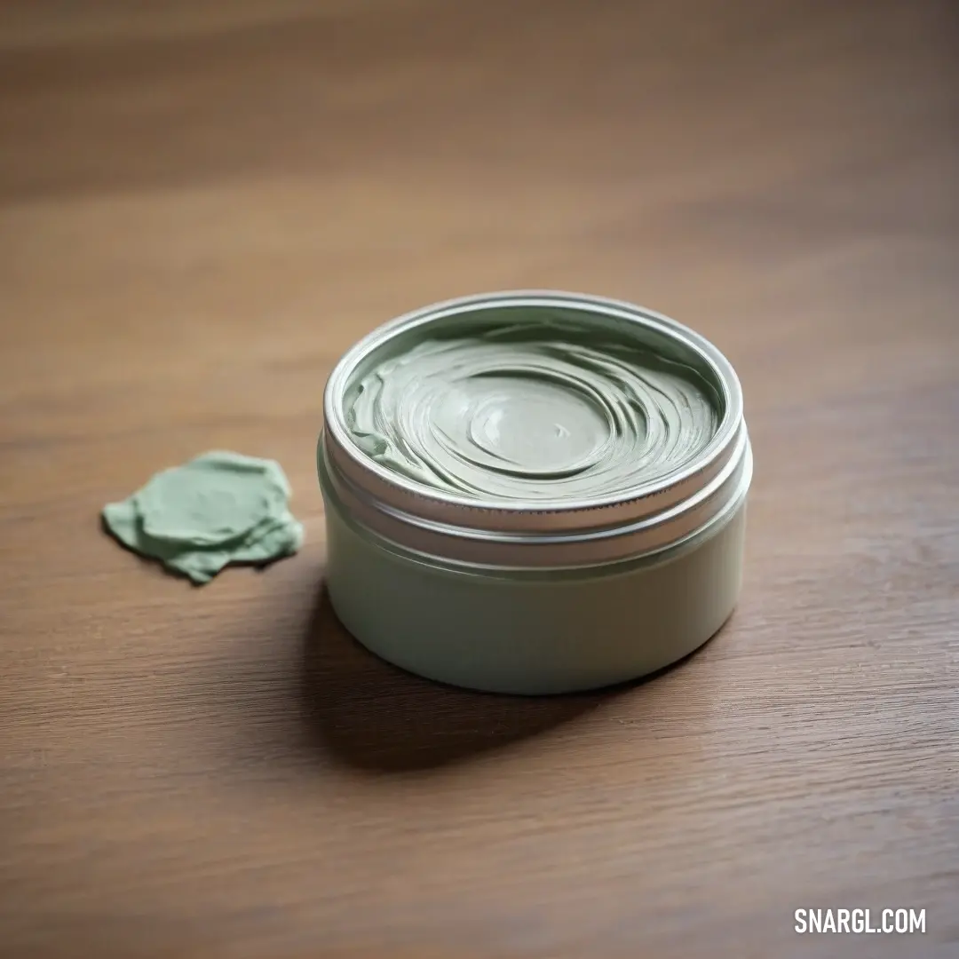 Jar of green cream on a table next to a small green object of wax on the table. Color CMYK 8,0,8,0.