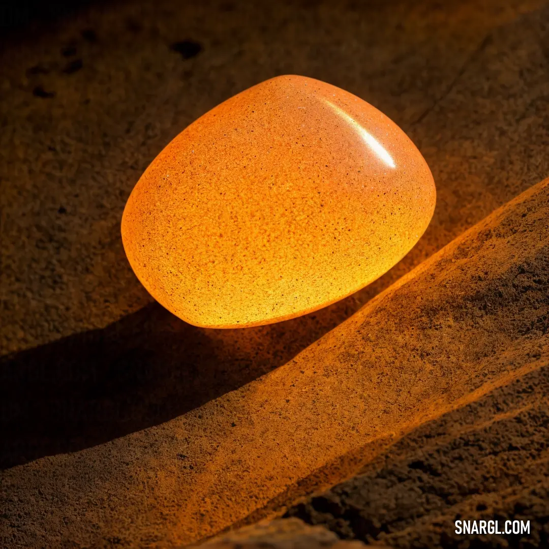 Yellow rock on top of a sandy beach next to a light bulb on a wall of sand. Color #F49A0A.