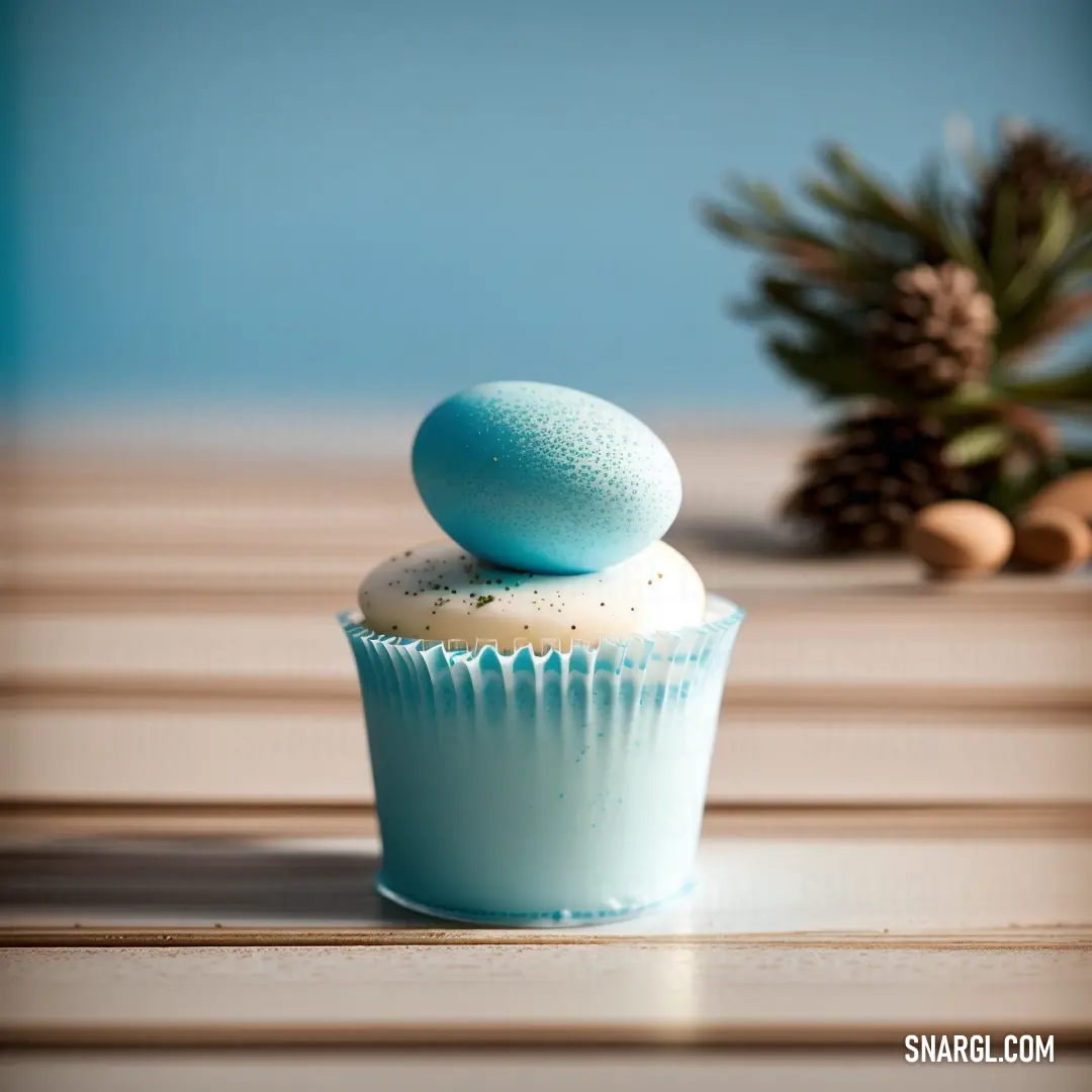 NCS S 1002-Y50R color. Cupcake with a blue frosting and a pine cone on the side of it on a table