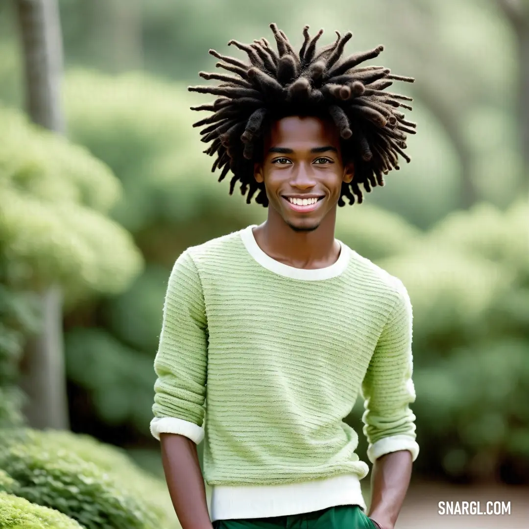 Man with dreadlocks standing in a park smiling for the camera with a green sweater on and green pants. Example of #DBF4BA color.