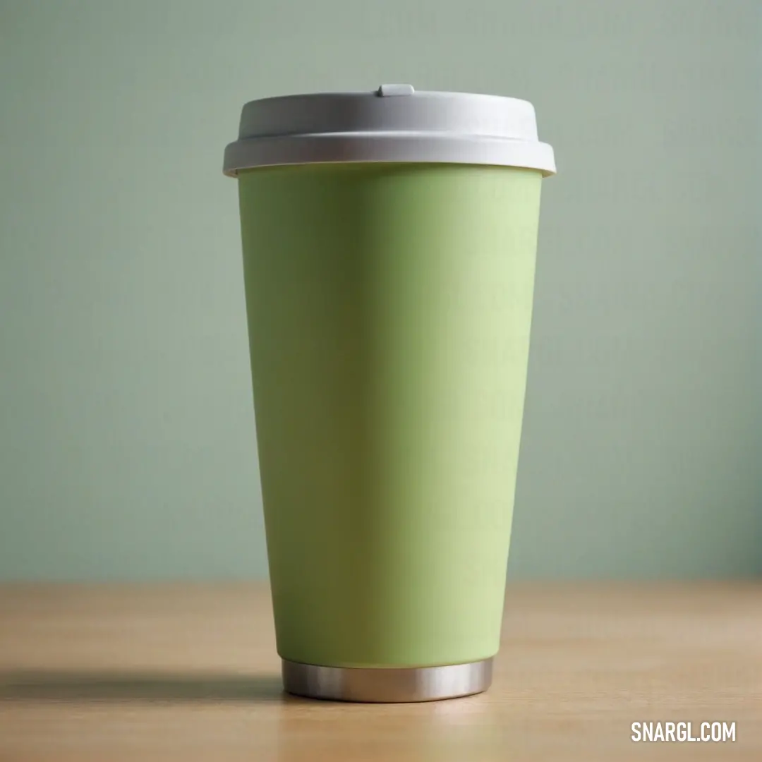Green cup with a white lid on a table with a green wall in the background. Example of RGB 201,238,159 color.