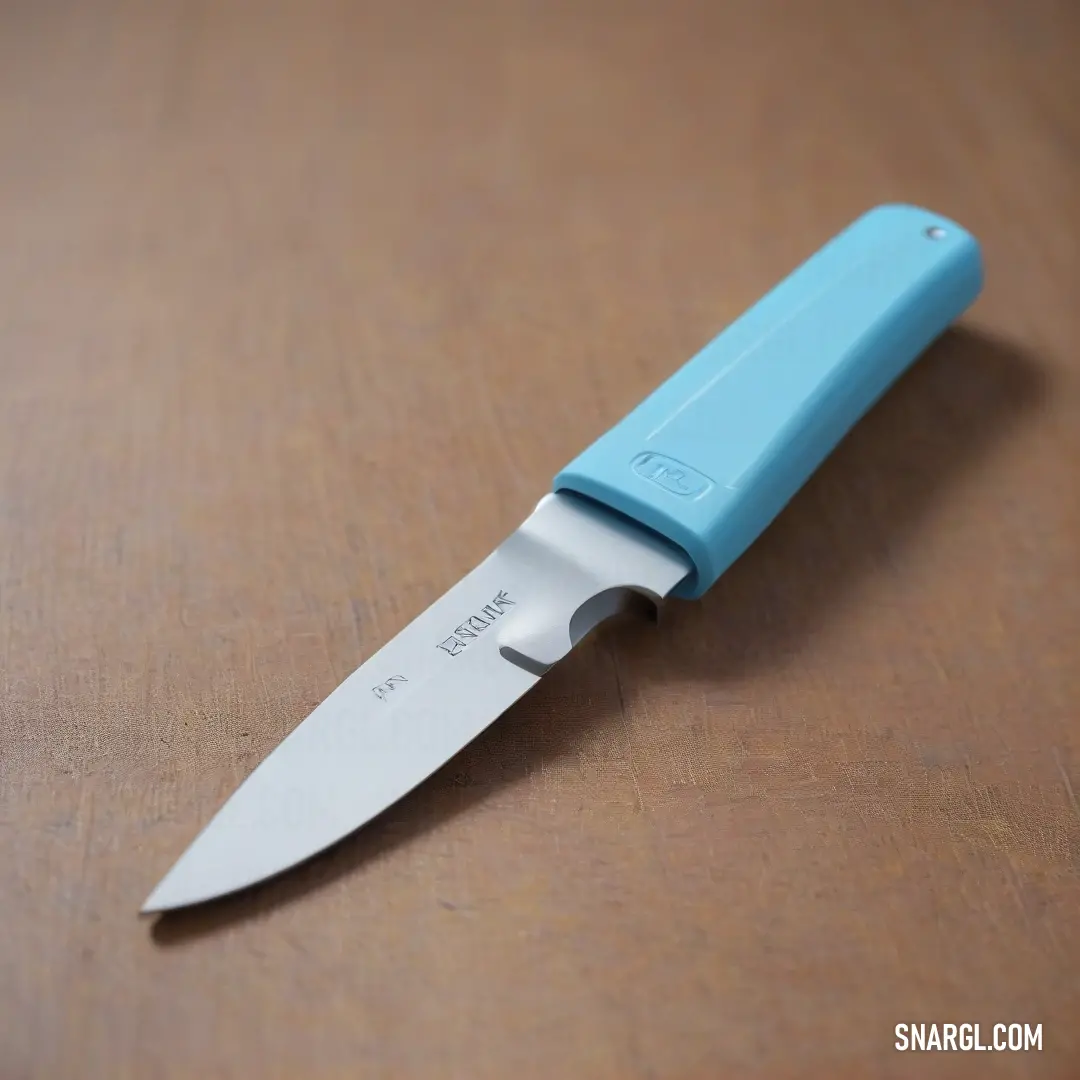 A blue knife with a sleek white handle rests on a rustic brown table, beautifully showcasing a combination of color and design that reflects the harmony of artistry and functionality in kitchen tools.