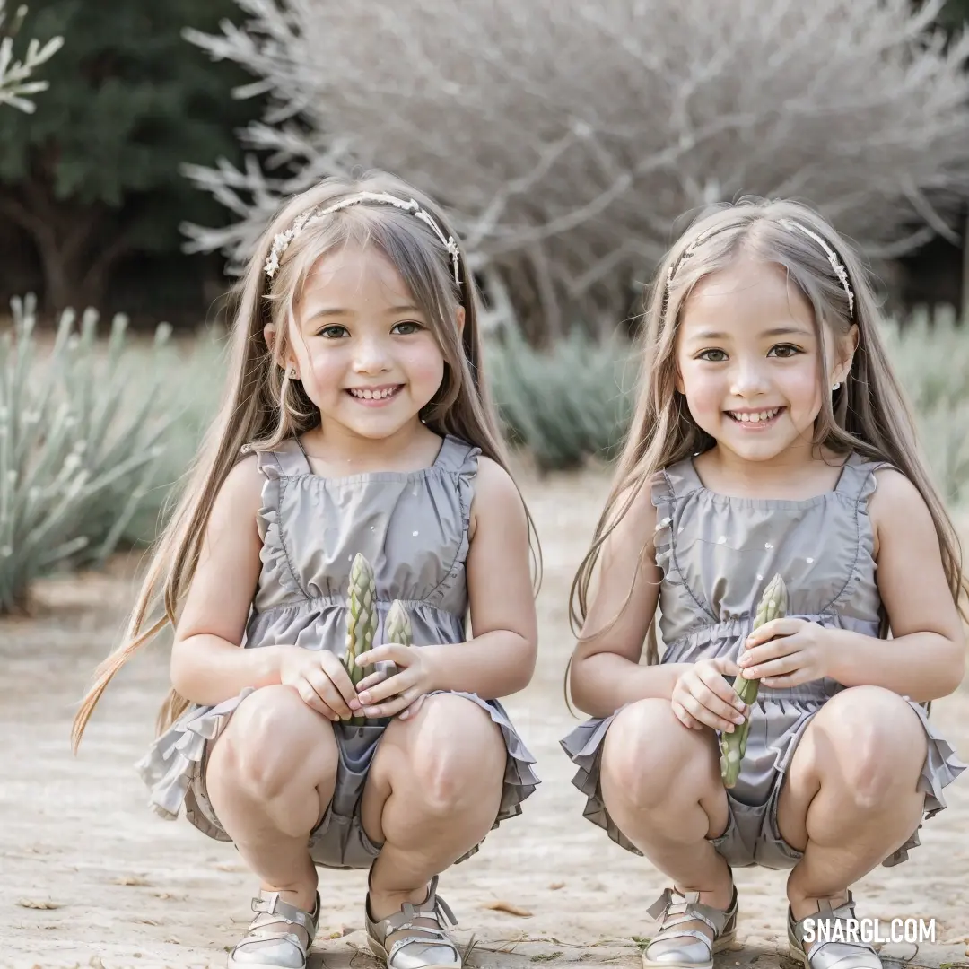 Two little girls on the ground with flowers in their hands and smiling at the camera. Color NCS S 2005-B80G.