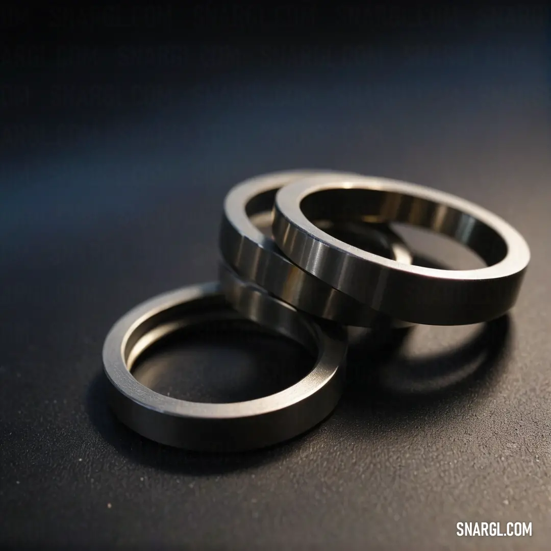 Two polished metal rings sit side by side on a sleek black tabletop, their reflective surfaces capturing light beautifully, creating a stunning visual contrast between the industrial design and the rich tones of the table beneath.