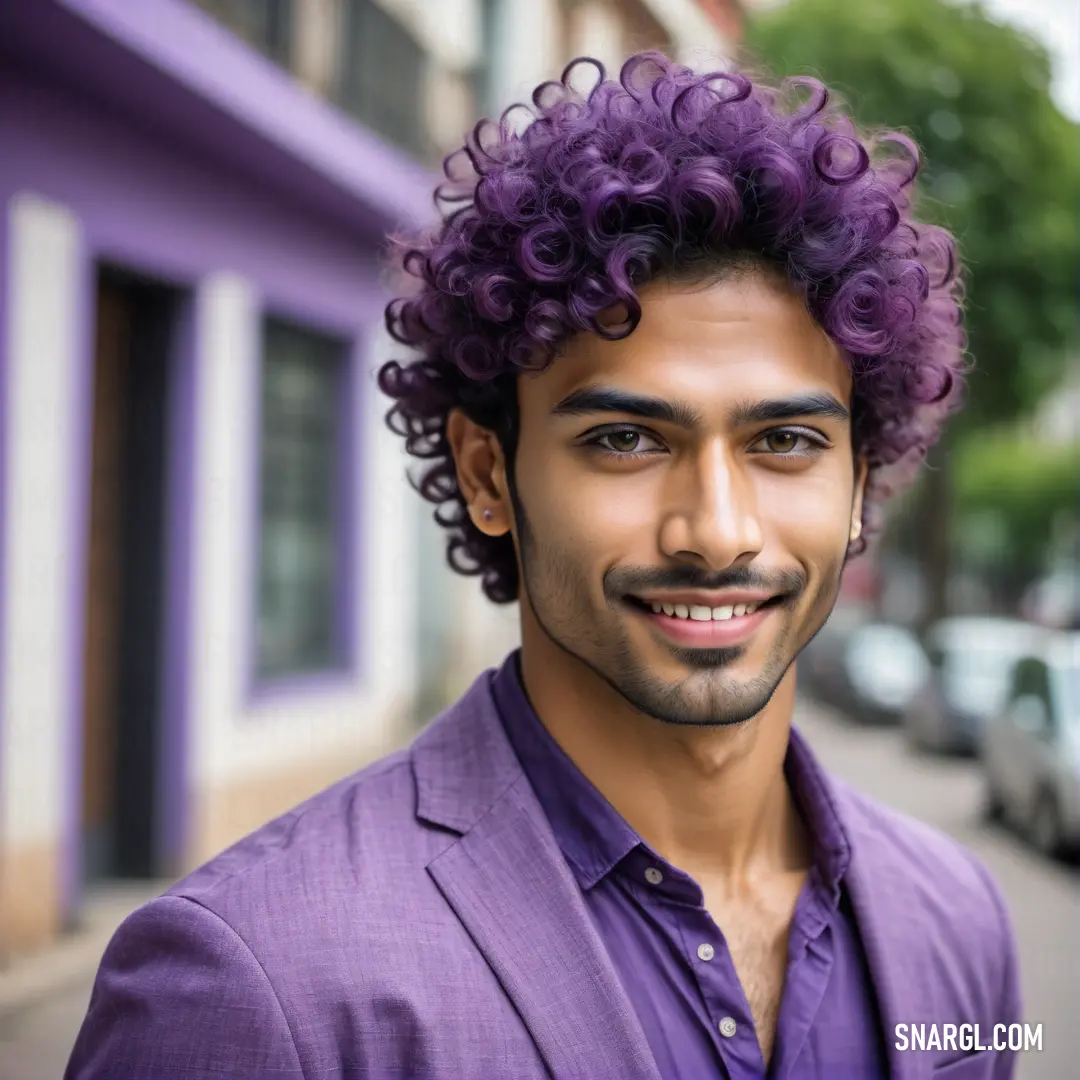 Man with a purple shirt and a purple jacket on a street corner with cars parked on the side of the street. Example of RGB 178,148,221 color.