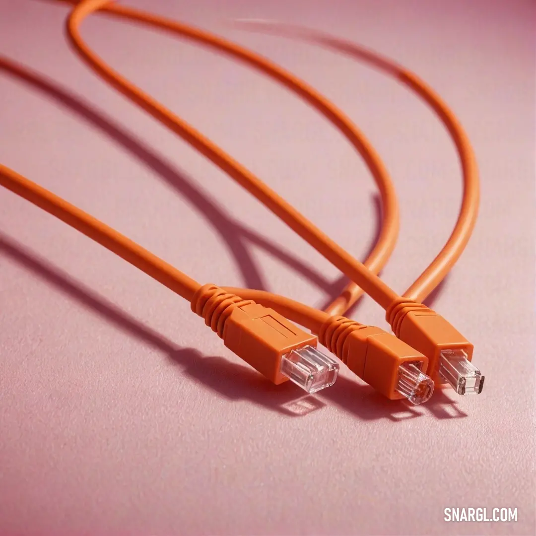 Two vibrant orange wires intertwine gracefully atop a soft pink surface, their texture and colors creating a playful visual dialogue. The pairing highlights the beauty in composition and the intricacies of everyday components.