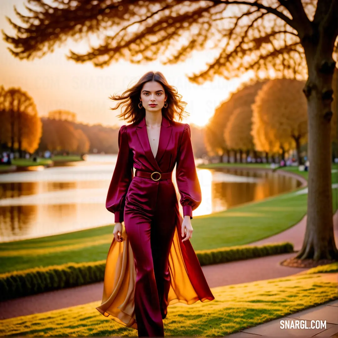 NCS S 2070-R10B color. Woman in a red suit walking down a sidewalk near a lake at sunset with a yellow bag in her hand