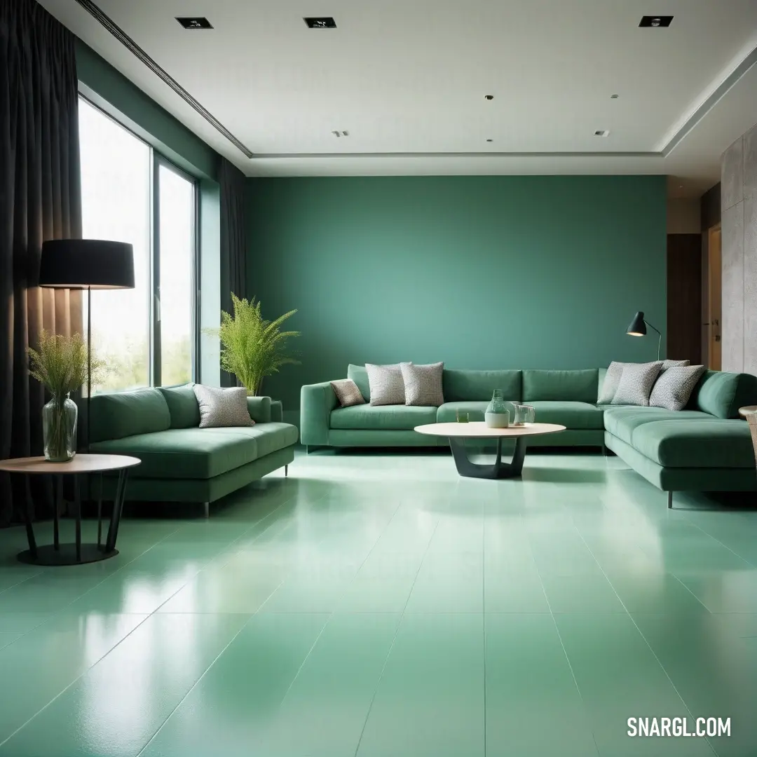Living room with a green couch and a table in it and a large window in the background. Color CMYK 52,0,38,45.