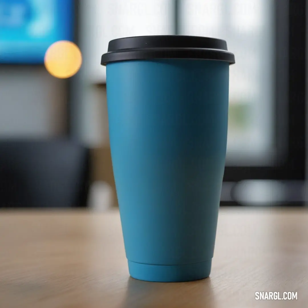 Blue cup on top of a wooden table next to a tv screen in a room with a black chair. Example of #005676 color.