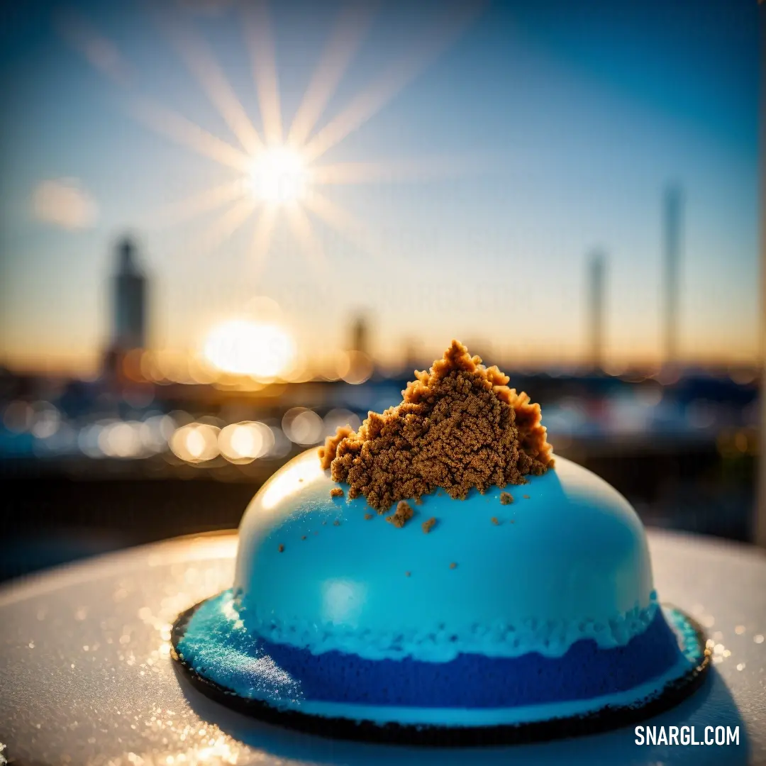 Blue cake with a brown crumb topping on top of it on a table in front of a city skyline. Color CMYK 0,55,95,45.