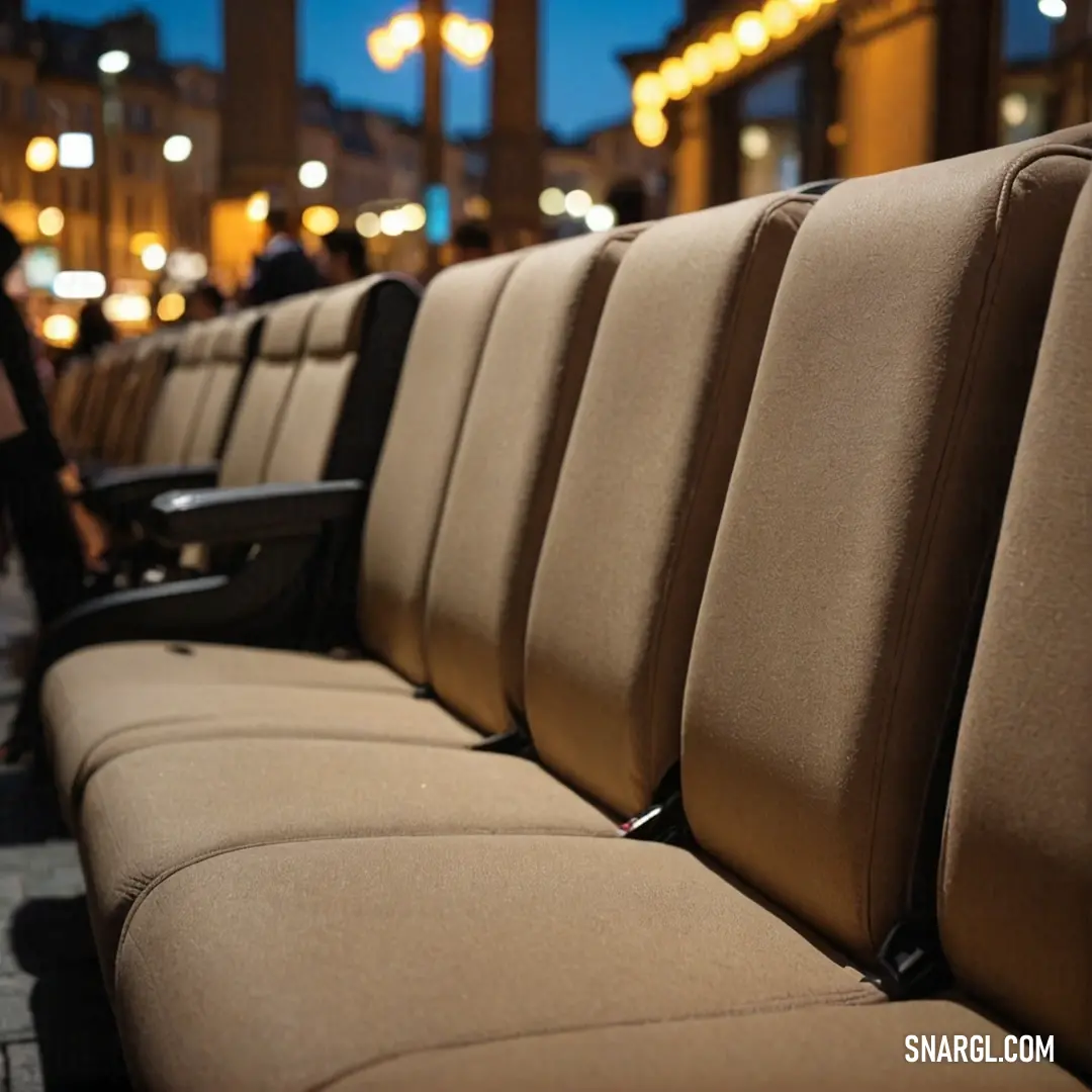 A picturesque nighttime scene with a row of stylish seats on a sidewalk, bustling with people in the background. The inviting atmosphere captures the essence of urban life and social engagement in a vibrant city setting.