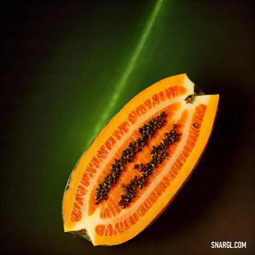 Cut in half papaya on a green surface with a black background and a green leaf behind it