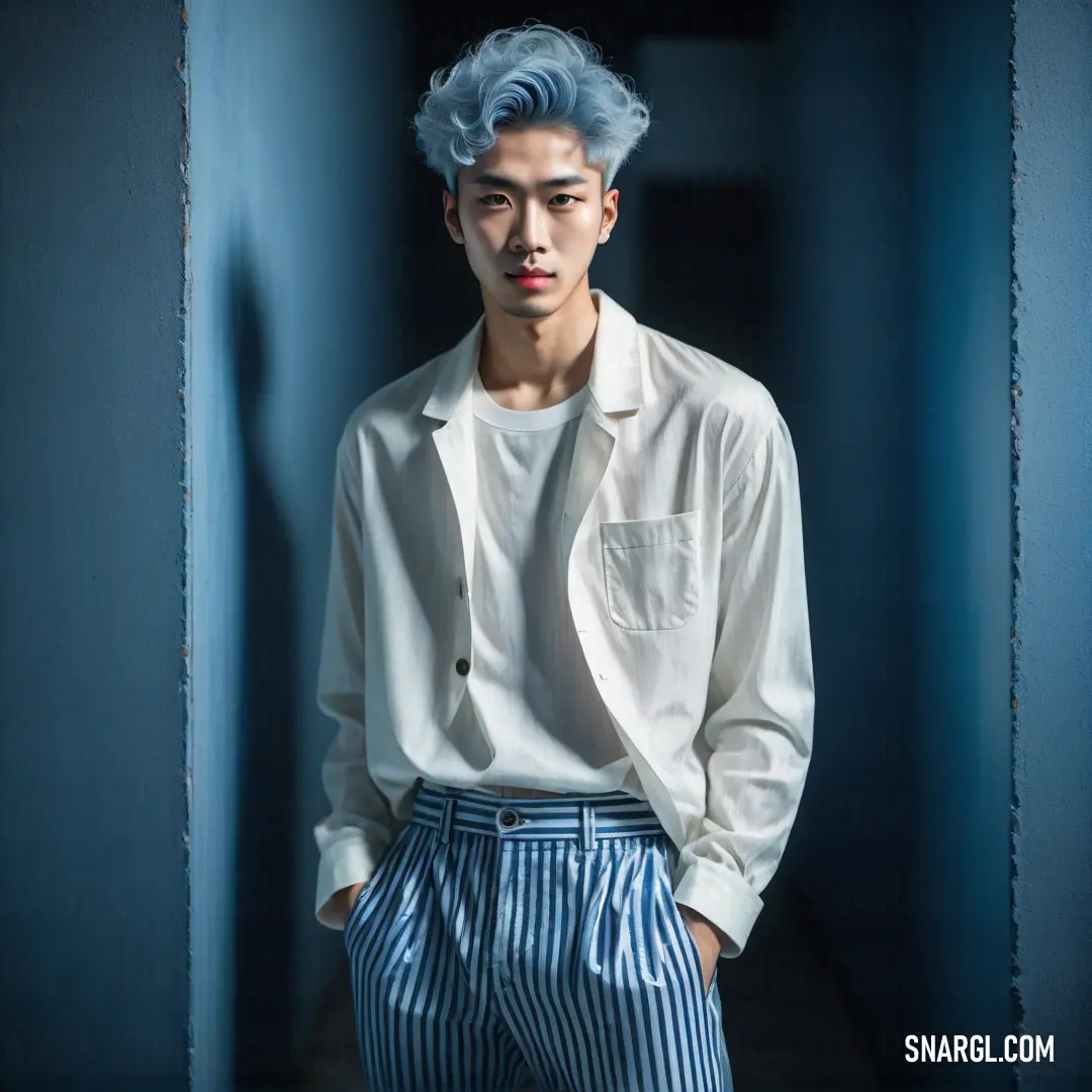 Man with blue hair standing in a hallway wearing a white shirt and blue striped pants