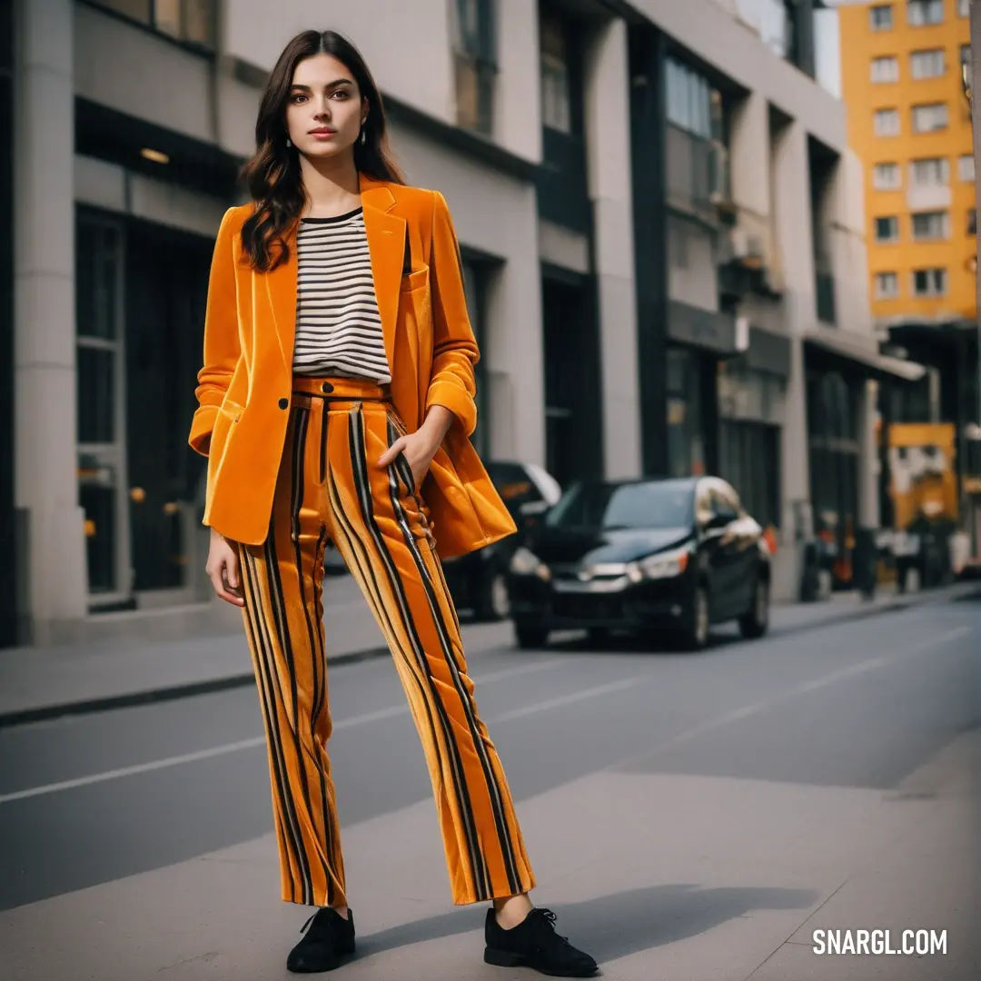 Woman in a yellow jacket and striped pants stands on a street corner in front of a building with cars
