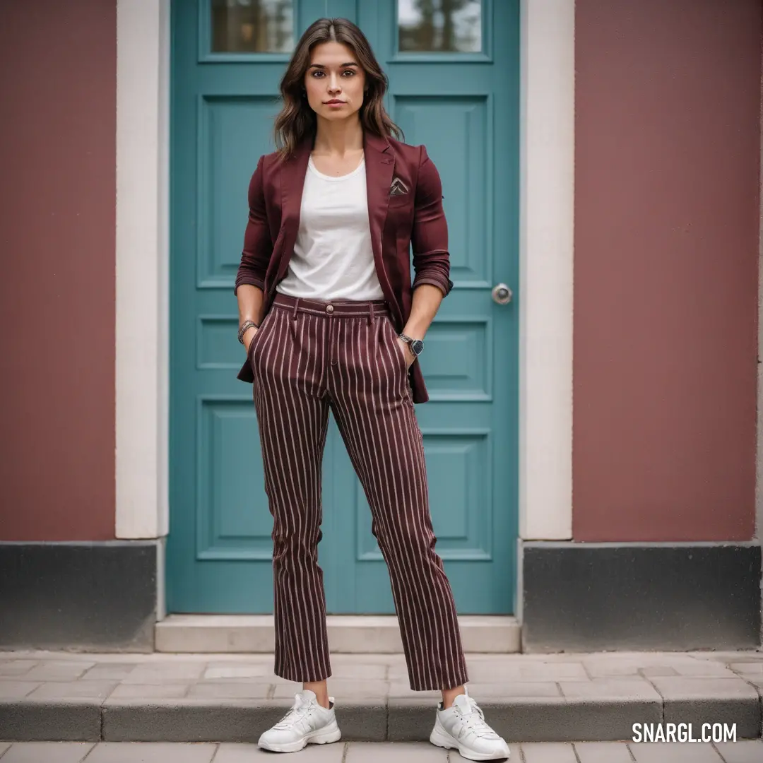 Woman standing in front of a blue door wearing a red jacket and striped pants with white sneakers on