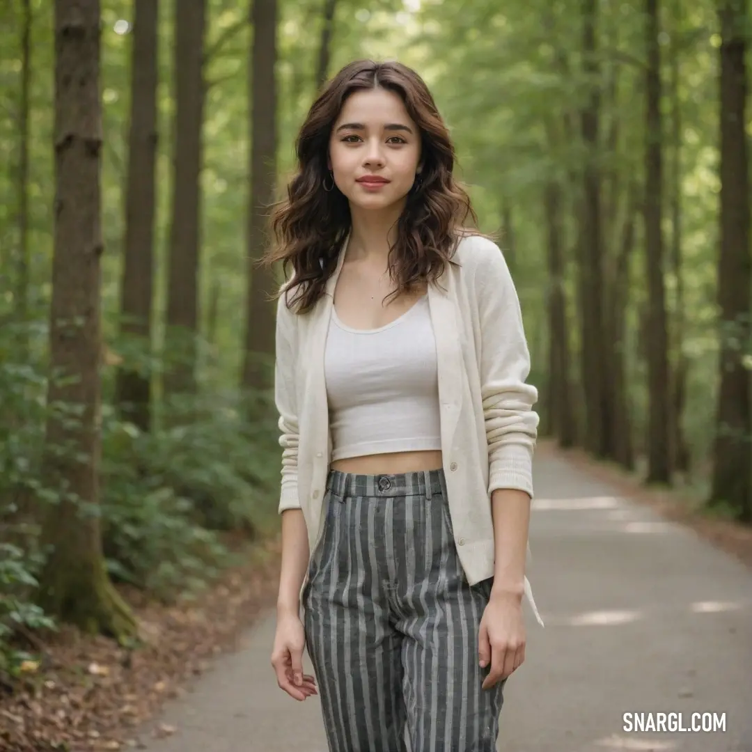Woman standing on a path in the woods wearing a white top and striped pants with a cardigan