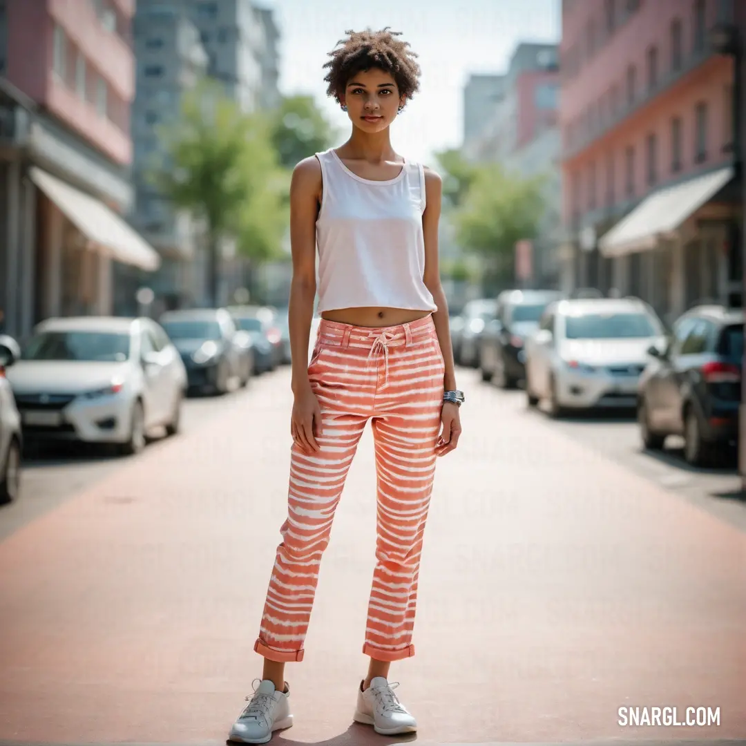 Woman standing on a sidewalk in a white top and orange pants with white sneakers on her feet