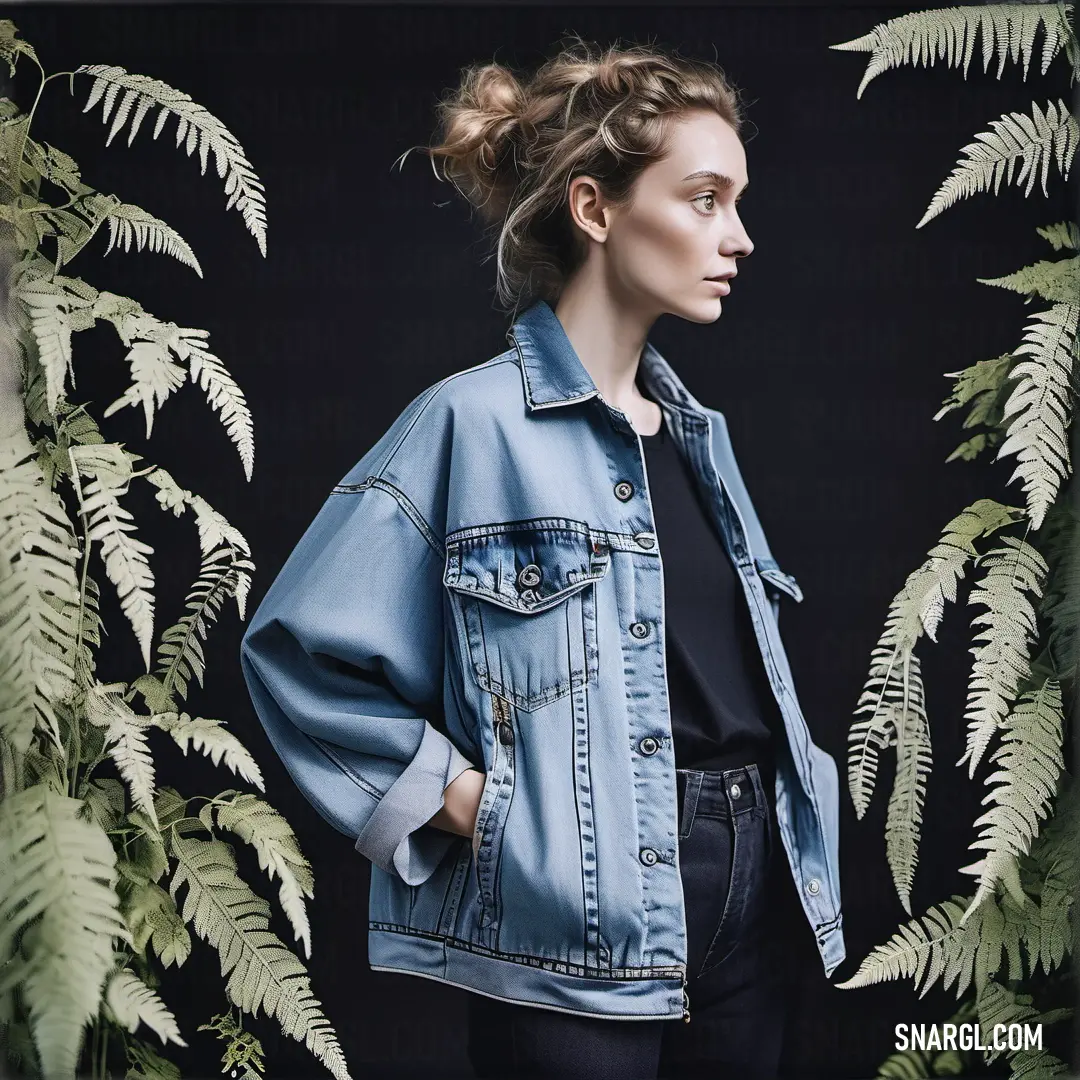 Woman in a denim jacket standing in front of a plant backdrop with fern leaves on it's sides