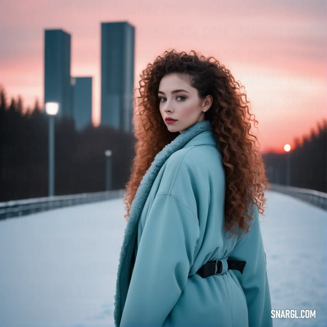 Woman with long red hair standing in the snow in front of a city skyline at sunset